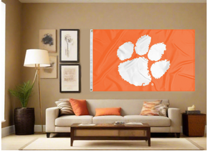 Orange 3x5 feet wide Clemson University Flag with White Paw and two metal grommets covering the tan wall inside of a well organized room with couch pillows and light