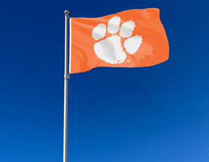 Orange 3x5 feet wide Clemson University Flag with White Paw and two metal grommets attached to flagpole waving in the wind