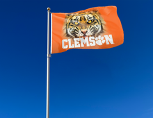 Load image into Gallery viewer, Quadruple Stitched Flyends of Orange 3x5 feet wide Clemson University Flag with realistic tiger face logo and Two Metal Grommets attached to flagpole waving in the wind

