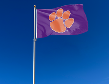 Load image into Gallery viewer, Purple 3x5 feet wide Clemson University Flag with Orange Paw and Two Metal Grommets attached to flagpole waving in the wind
