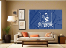 Load image into Gallery viewer, Blue 3x5 foot wide Duke University Flag with Duke Logo Blue Devils Logo and two metal grommets covering the tan wall of the living room
