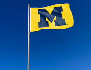 Gold 3x5 foot wide University of Michigan Flag with two metal grommets attached to flagpole waving in the wind
