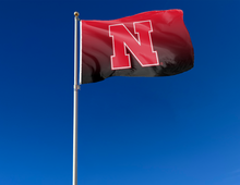 Load image into Gallery viewer, Gradient University of Nebraska Flag with two metal grommets attached to flagpole waving in the wind
