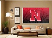 Load image into Gallery viewer, Gradient 3x5 foot wide University of Nebraska Flag with two metal grommets covering the tan wall of a well-lit room
