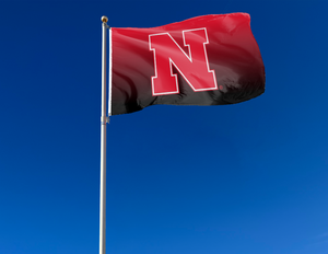 Gradient 3x5 foot wide University of Nebraska Flag with two metal grommets attached to flagpole waving in the wind