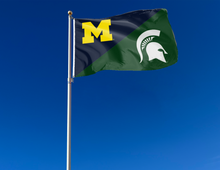 Load image into Gallery viewer, blue and green Michigan MSU House divided with Spartan Helmet Logo attached to flagpole waving in the wind

