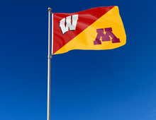 Load image into Gallery viewer, red and gold Wisconsin Minnesota House Divided Flag with two metal grommets attached to flagpole waving in the wind

