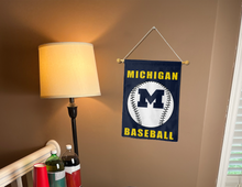 Load image into Gallery viewer, blue Michigan Baseball garden flag hung on a banner pole next to a lamp and drinks.

