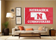Load image into Gallery viewer, Nebraska Cornhuskers flag with state of Nebraska border logo hung inside a well-lit living room
