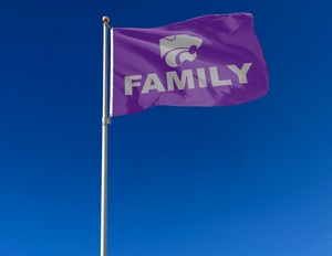 Purple 3x5 foot wide Kansas State University flag with grey Family logo and two metal grommets attached to flagpole waving in the wind