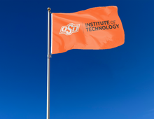 Load image into Gallery viewer, Orange Oklahoma State University Institute of Technology Flag with two metal grommets attached to flagpole waving in the wind
