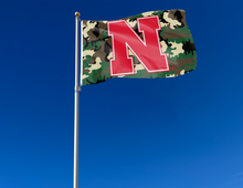 Load image into Gallery viewer, Camo 3x5 University of Nebraska Flag with Red N and two metal grommets attached to flagpole waving in the wind
