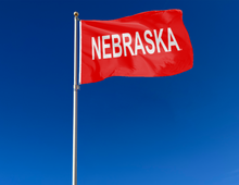 Load image into Gallery viewer, red Nebraska huskers flag with Nebraska wordmark logo attached to flagpole waving in the wind
