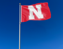 Load image into Gallery viewer, Red Nebraska Huskers Flag attached to flagpole waving in the wind
