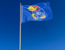 Load image into Gallery viewer, Blue 3x5 foot wide University of Kansas Flag with Jayhawks logo and two metal grommets attached to flagpole waving in the wind
