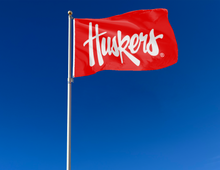 Load image into Gallery viewer, Outdoor display of Nebraska Huskers Flag with white Huskers script font logo
