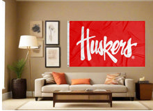 Load image into Gallery viewer, Red University of Nebraska Flag with white Huskers script font logo inside well-lit room

