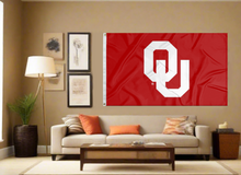 Load image into Gallery viewer, Red 3x5 feet wide University of Oklahoma Flag with two metal grommets for indoor home decor covering tan wall of well lit room
