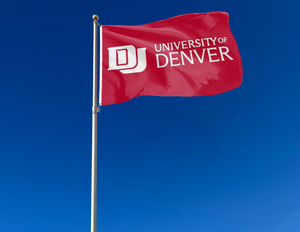 Red 3x5 foot wide University of Denver  Flag with white school logo and two metal grommets attached to flagpole waving in the wind