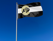 Load image into Gallery viewer, State of Colorado Style University of Colorado Flag with three black white and black horizontal stripes and Gold C Logo filled with Buffaloes logo On top of the stripes and two metal grommets attached to flagpole waving in the wind

