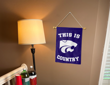 Load image into Gallery viewer, purple kansas state university garden flag with this is country logo hung on banner pole next to lamp and drinks
