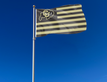 Load image into Gallery viewer, 3x5 feet wide University Of Colorado Flag with thirteen black and gold stripes and two metal grommets attached to flagpole waving in the wind with blue sky background

USA Flag Style University of Colorado Flag
