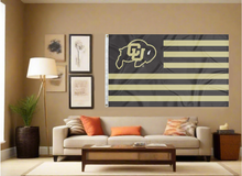 Load image into Gallery viewer, 3x5 feet wide University Of Colorado Flag with thirteen black and gold stripes and two metal grommets covering the tan wall inside of a well organized room with couch pillows and light
