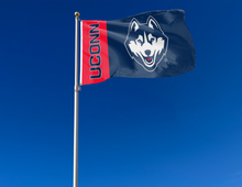 Load image into Gallery viewer, 2 Panel Red and navy 3x5 foot University of Connecticut (UCONN) Huskies 2 Panel 3x5 Flag with two metal grommets attached to flagpole waving in the wind
