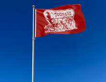 Load image into Gallery viewer, Red 3x5 feet wide University of Oklahoma Sooners Flag with Sooners Wagon Logo and two metal grommets for outdoor home decor attached to flagpole waving in the wind
