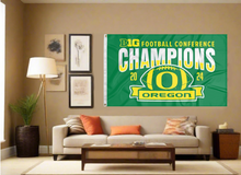 Load image into Gallery viewer, 3x5 foot Green University of Oregon Football BIG Ten Football Championship 2024 Champions Flag with two metal grommets covering a tan wall with a living room above the gray couch 
