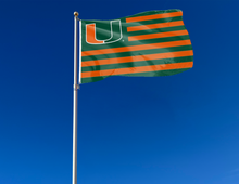 Load image into Gallery viewer, outdoor display of miami hurricanes flag with seven green and six orange stripes as part of tailgate decor
